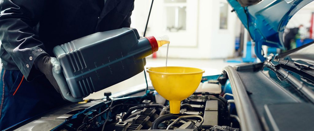 Mechanic pouring motor oil into a yellow funnel, emphasizing the importance of regular oil changes for vehicle maintenance.