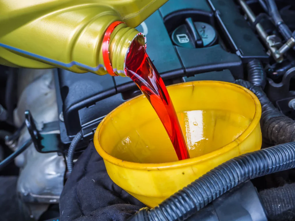Pouring bright red transmission fluid into a yellow funnel, highlighting essential vehicle maintenance for transmission service at Guaranteed Auto Air & Repair in Rockledge, FL.